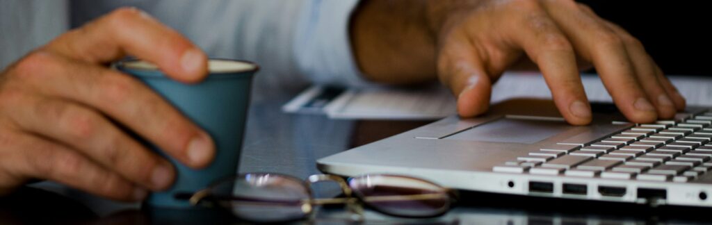 Person holding ceramic mug while working on laptop
